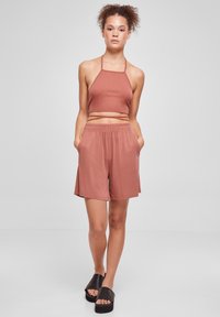Hnědou ribbovanou halter crop top s odpovídajícími šortkami s elastickým pasem, které mají boční kapsy. Modelka má na sobě černé sandály na klínku.