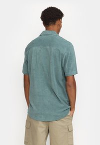Korte mouwen, turquoise shirt van textuurstof, met een klassieke kraag en rugdetail. Gepaard met khaki cargoshorts.