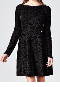 Svart sammetsklänning med långa ärmar. Har ett blommönstrat spetsmönster och en figurnära överdel som vidgar sig vid midjan.