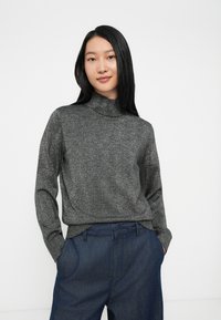 Suéter cinza metálico de gola alta com mangas longas e punhos canelados, combinado com calças de cintura alta de cor azul-escuro. Tecido suave e texturizado.