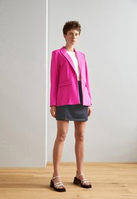 Rosa blazer med to frontlommer, hvit t-skjorte under, mørk denimskjørt og beige hælsandaler. Glatt materiale, moderne snitt.
