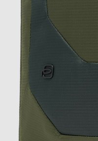 Donkergroene, textuurrijke stoffen pouch met een glad accentontwerp en een zwart logo. Het materiaal heeft een lichte glans, wat duidt op duurzaamheid.