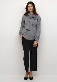Blusa a righe con collo a fiocco grigio e bianco, abbinata a pantaloni neri a gamba larga. Scarpe nere basse completano il look.