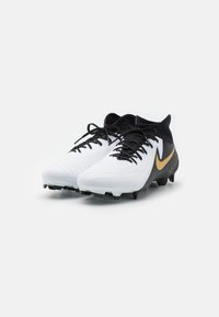 Baltas un melns futbola apavi ar teksturētu dizainu, ar izteiktu zeltītu Nike simbolu un melnām auklām. Moldēti gumijas tapu bloki zolei.