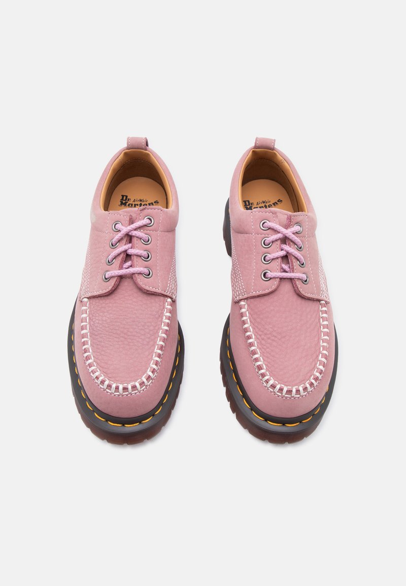 Coppia di mocassini rosa in pelle con punta arrotondata, suole nere spesse, cuciture bianche, lacci e linguette di tiraggio, vista dall'alto su sfondo bianco.