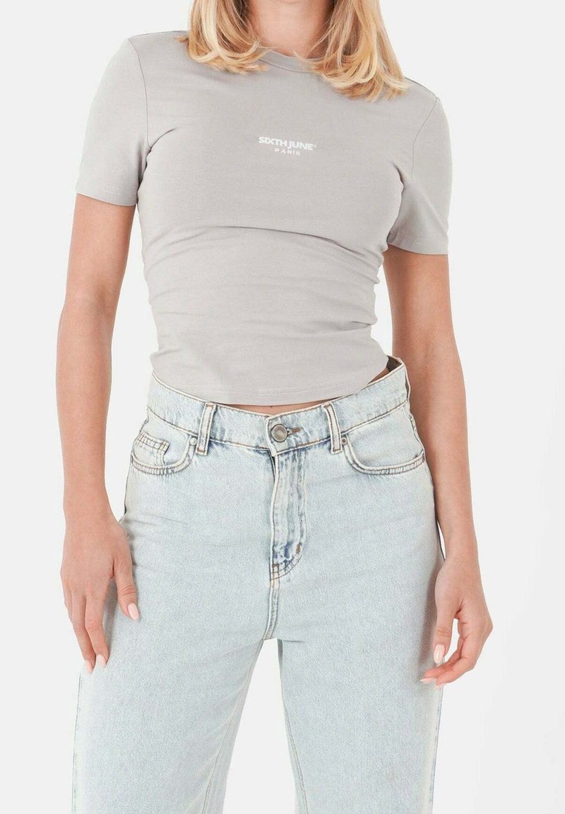 T-shirt gris ajusté à manches courtes avec logo blanc ; associé à un jean taille haute bleu clair avec une coupe classique à cinq poches.