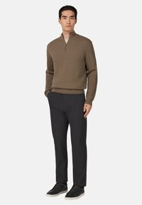 Brązowy sweter z dzianiny z rozpinanym kołnierzem, w połączeniu z czarnymi dopasowanymi spodniami i czarnymi sneakersami. Strój ma fakturowany wzór.