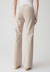Beige Wellencord-Flared-Hosen von hinten gezeigt. Verfügt über zwei Gesäßtaschen, strukturierten Stoff und ein unauffälliges Taillenlabel.