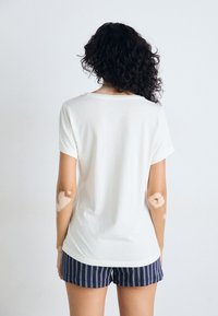 Camiseta branca de manga curta com um corte descontraído, combinada com calções às riscas azuis e brancas. A camisa tem uma textura suave e um decote arredondado.