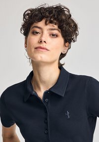 Marinblå pikétröja i strukturerad tyg med klassisk krage, treknappsstängning och en liten broderad logotyp på bröstet.