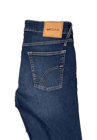 Jeans de mezclilla azul oscuro con una etiqueta de cuero que muestra "GAS". Cuenta con detalles de costura y un diseño distintivo en el bolsillo trasero.