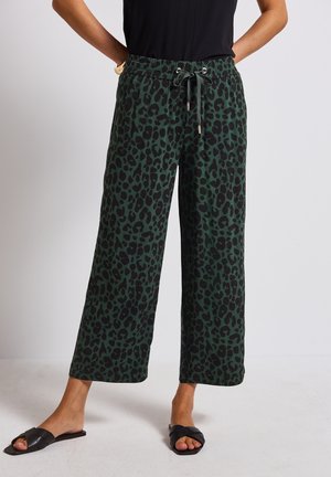 Green and black leopard print wide-leg pants with an elastic waistband and drawstring. Paired with black slide sandals.