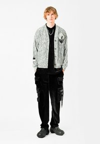 Cardigan gris con textura y un parche, camiseta negra y pantalones cargo de terciopelo negro. Combinado con zapatos negros de diseño.