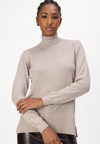 Bež turtleneck pulover od mekog pletenog materijala, s dugim rukavima, rebrastim manžetama i blago produženim rubom s bočnim prorezima.