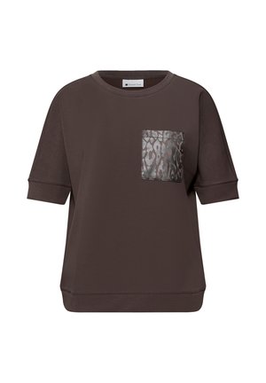 Hnědá mikina s krátkými rukávy vyrobená z měkké tkaniny, s šedým metalickým skvrnitým nášivkou na levé straně hrudi. Volný střih.