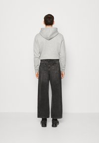 Harmaa huppari, jossa on rento istuvuus, yhdistettynä leveisiin tummanharmaisiin farkkuihin. Asusteessa on minimalistinen muotoilu ilman näkyviä kuvioita.