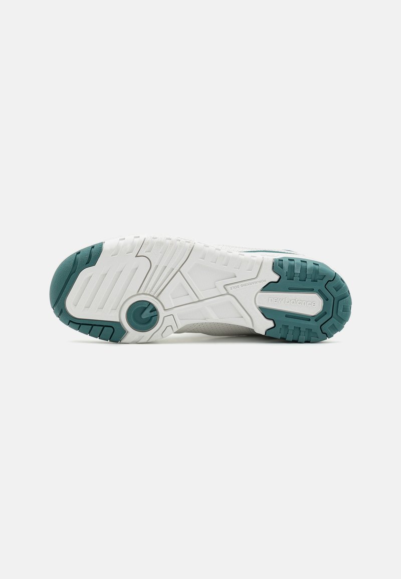 Semelle de chaussure de sport blanche et turquoise présentant plusieurs motifs de traction, en caoutchouc texturé, avec un accent circulaire près du centre.