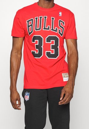 Mężczyzna w czerwonej koszulce Chicago Bulls z numerem 33 i czarnych spodniach z logo NFL na górnej części uda, stojący na białym tle.