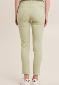 Pantaloni in cotone verde chiaro con una vestibilità slim, dotati di tasche posteriori e una texture liscia. Abbinati a sneakers bianche con dettagli dorati.