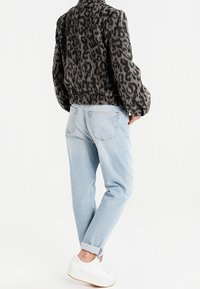 Giacca in pelliccia sintetica con stampa leopardata e polsini arricciati, abbinata a jeans tapered blu chiaro e sneakers bianche.