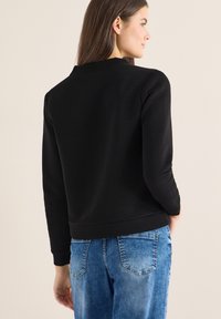 Felpa nera a coste con scollo rotondo, maniche lunghe e vestibilità rilassata, abbinata a jeans di denim azzurro chiaro.