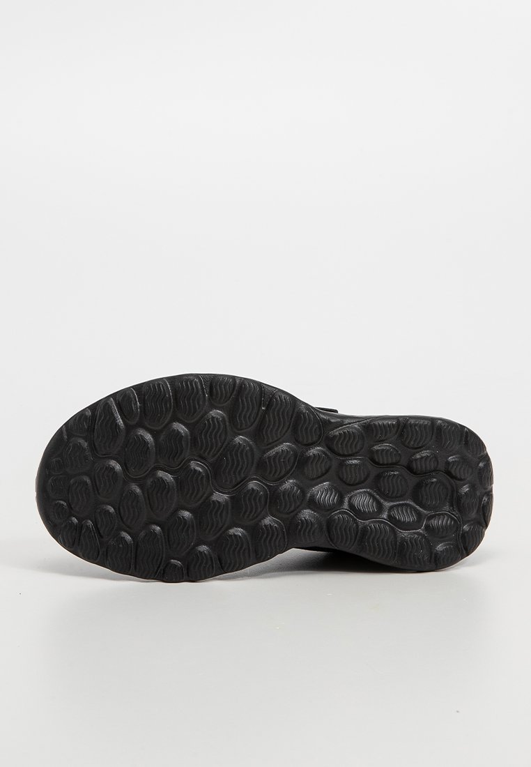 Semelle de sneaker noire en caoutchouc texturé, dotée d'une forme arrondie et de motifs circulaires pour une meilleure adhérence. Conçue pour assurer une traction sur diverses surfaces.