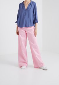 Blusa azzurro chiaro, morbida eamp;nbsp;con scollo a V e maniche arricciate; abbinata a pantaloni larghi rosa chiaro e sneakers bianche.