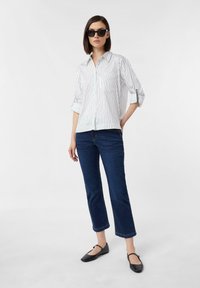 White and blue striped button-up shirt with rolled sleeves, paired with dark blue cropped jeans and black flats. Clear sunglasses complete the look.