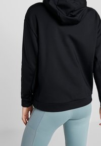 Felpa nera con cappuccio, dal taglio comodo, realizzata in tessuto morbido e con polsini a coste. Abbinata a leggings azzurri chiari con pannelli laterali testurizzati.
