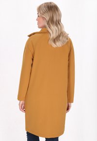 Gelinės geltonos spalvos trenčkotai su laisvu siluetu, ilgomis rankovėmis ir nugaros ventiliacija. Lygus audinys, paprastas dizainas ir be matomų detalių.