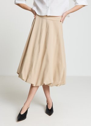 Jupe beige mi-longue au design fluide avec une texture lisse. Portée avec des chaussures noires à enfiler à bout pointu.