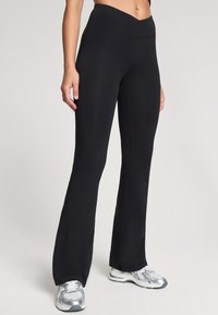 Czarne legginsy dzwonowe wykonane z elastycznego materiału, z wysokim pasem w kształcie litery V, gładką teksturą i subtelnymi detalami w szwach.