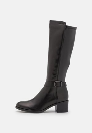 Botte en cuir noire montant jusqu'au genou avec talon bloc bas et bride décorative avec boucle sur fond gris clair.