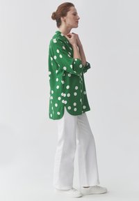 Cămașă verde cu buline cu guler și manșete până la trei sferturi, asortată cu pantaloni albi cu croială largă și teniși albi. Textură de țesătură netedă.