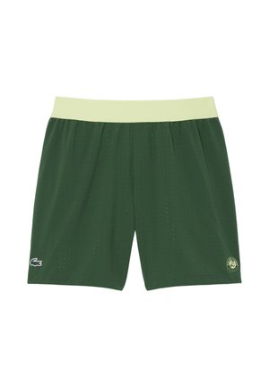 Pantalones cortos deportivos perforados de color verde oscuro con cintura de color verde claro, logo del cocodrilo de Lacoste en la pierna izquierda y emblema de Roland Garros en la pierna derecha.