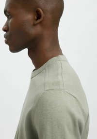 Vaaleanvihreä neulepaita, jossa on ribbineulottu kaula-aukko ja olkasaumat. Paita on slim fit -mallinen ja siinä on sileä pinta.