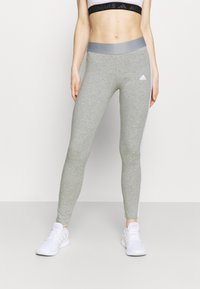 Ljusgrå idrottsleggings med en slät textur, med en kontrasterande grå midja och vita sidostråkar. Varumärkeslogotyp på benet.