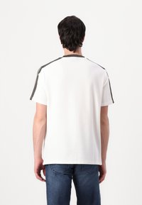 Vit t-shirt med kort ärm och en solid design, kontrasterande mörkgrå axelinslag, och rundad halsringning, tillsammans med blå jeans.