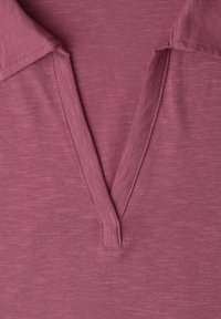 Plan rapproché d'un tissu tricoté rose avec col en V et détails de couture visibles.