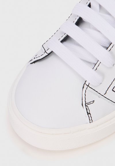 Vita lädersneakers med vita snören, med kontrasterande svart sömnad och en strukturerad gummisula. Designen inkluderar geometriska detaljer.