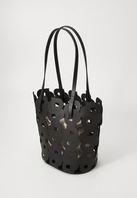 Bolso tote negro con diseño recortado que presenta patrones circulares, asas de cuero y un forro interior brillante. Forma estructurada y de apertura superior.
