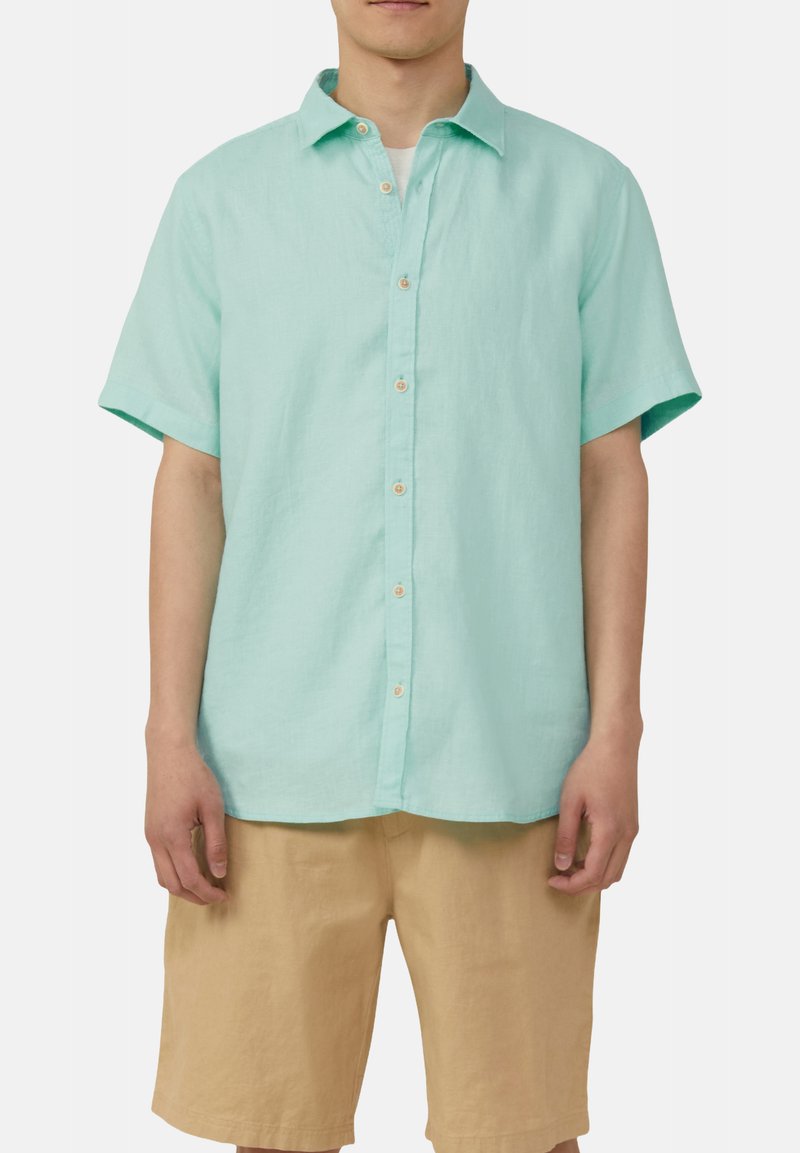 Lichtblauw overhemd met korte mouwen van linnen, voorzien van een kraag, een relaxte pasvorm en subtiele witte knopen. Gecombineerd met beige shorts.