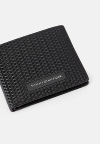 Čierna tkaná peňaženka s textúrovaným povrchom, s obdĺžnikovým logom Tommy Hilfiger v bielej farbe na čiernom koženom akcentu.