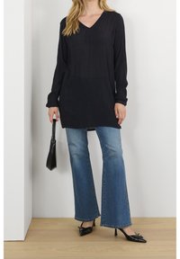 Sort tunika med lange ærmer og V-hals, kombineret med lyseblå vide jeans og sorte spidse hæle. Enkel håndtaske i hånden.