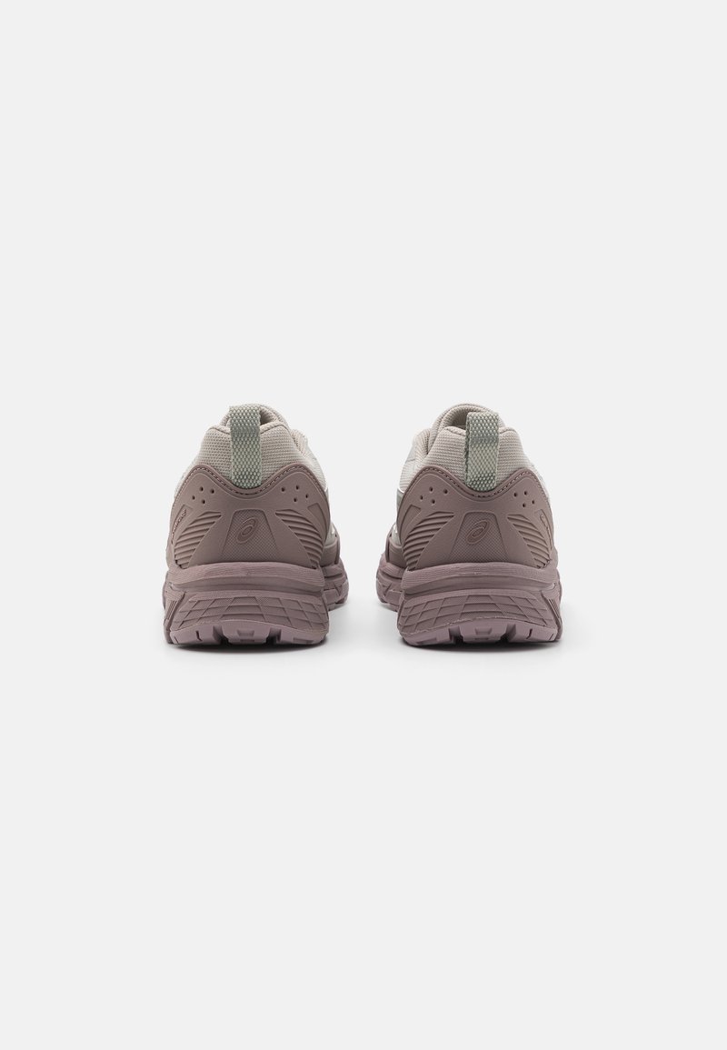 Des chaussures de sport avec une tige en tissu texturé marron et gris, dotées d'une languette verte à l'arrière et d'une semelle en caoutchouc rainurée pour plus de traction.