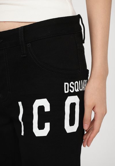 Zwarte denim jeans met witte geborduurde letters "DSQUARED" en "ICO." De stof heeft een gladde textuur, met vijf zakken en een fitted ontwerp.