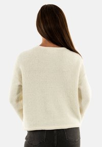 Maglione bianco e peloso con scollatura rotonda, maniche lunghe e lunghezza corta. L'orlo presenta un sottile motivo cucito.