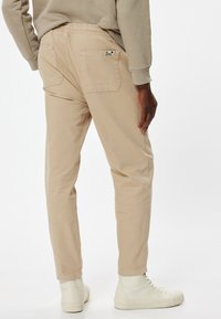Beige bomuldsbukser med elastisk talje, to baglommer og taperede ben. Stylet med hvide sneakers i høj topl. 