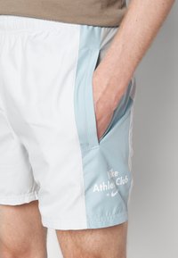 Shorts de sport Nike blancs et bleu clair avec poches latérales, ceinture élastique et détails de logo imprimés sur la jambe gauche.