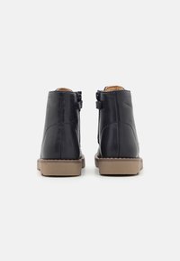 Bottes chelsea en cuir marine avec une texture lisse et des zips sur le côté. Semelles en caoutchouc beige. Design simple sans motifs ou accents supplémentaires.